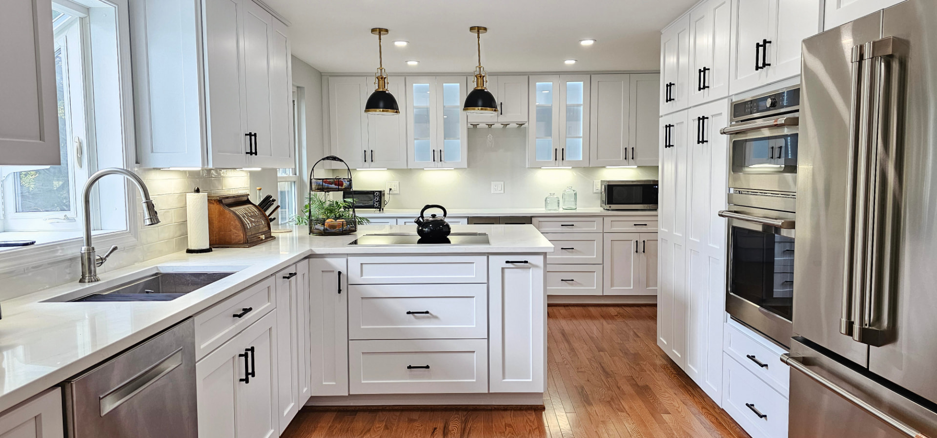 White kitchen with induction peninsula, brass pendants, and built-in wall ovens