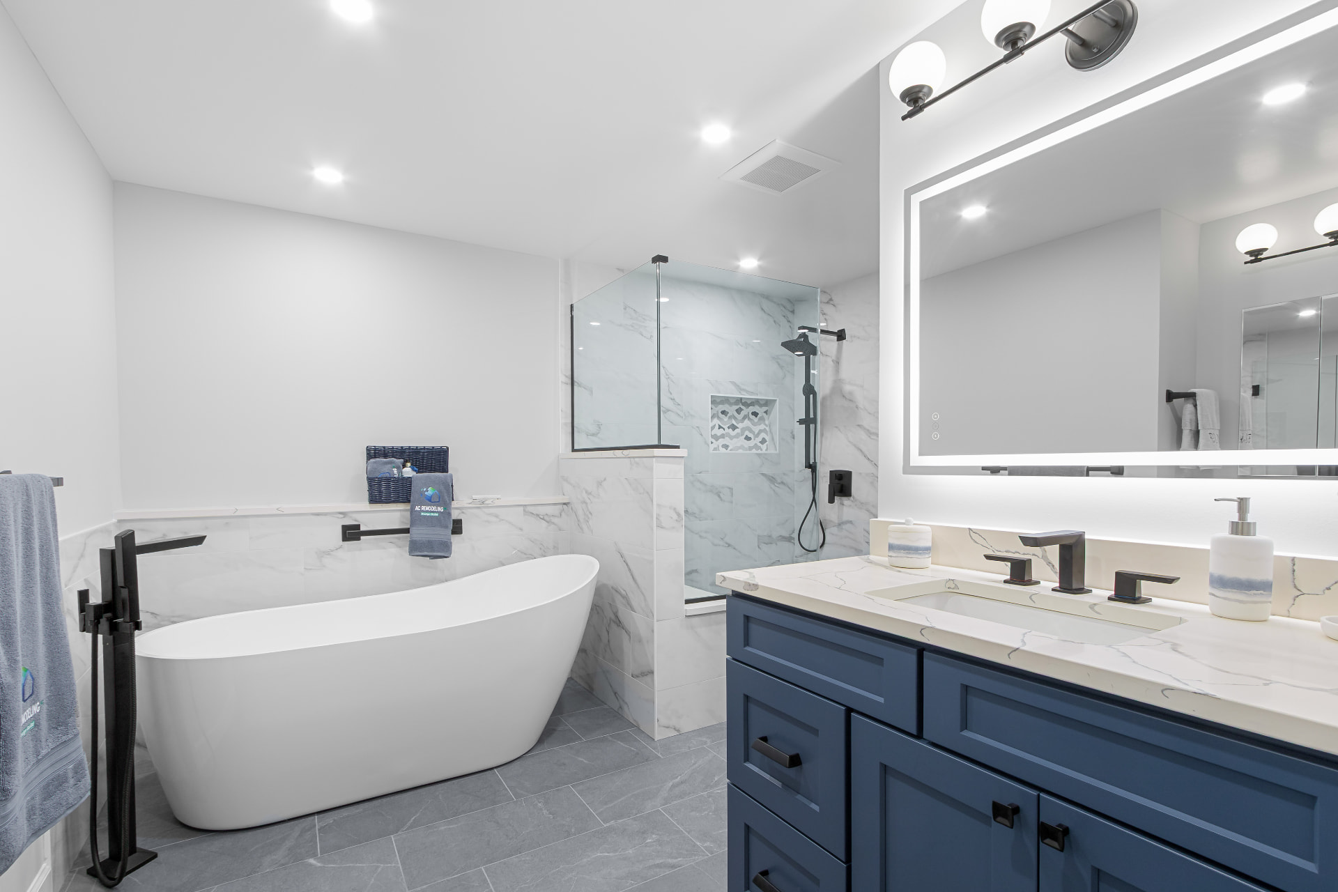 Primary bath with freestanding tub, navy blue double vanity and backlit mirror
