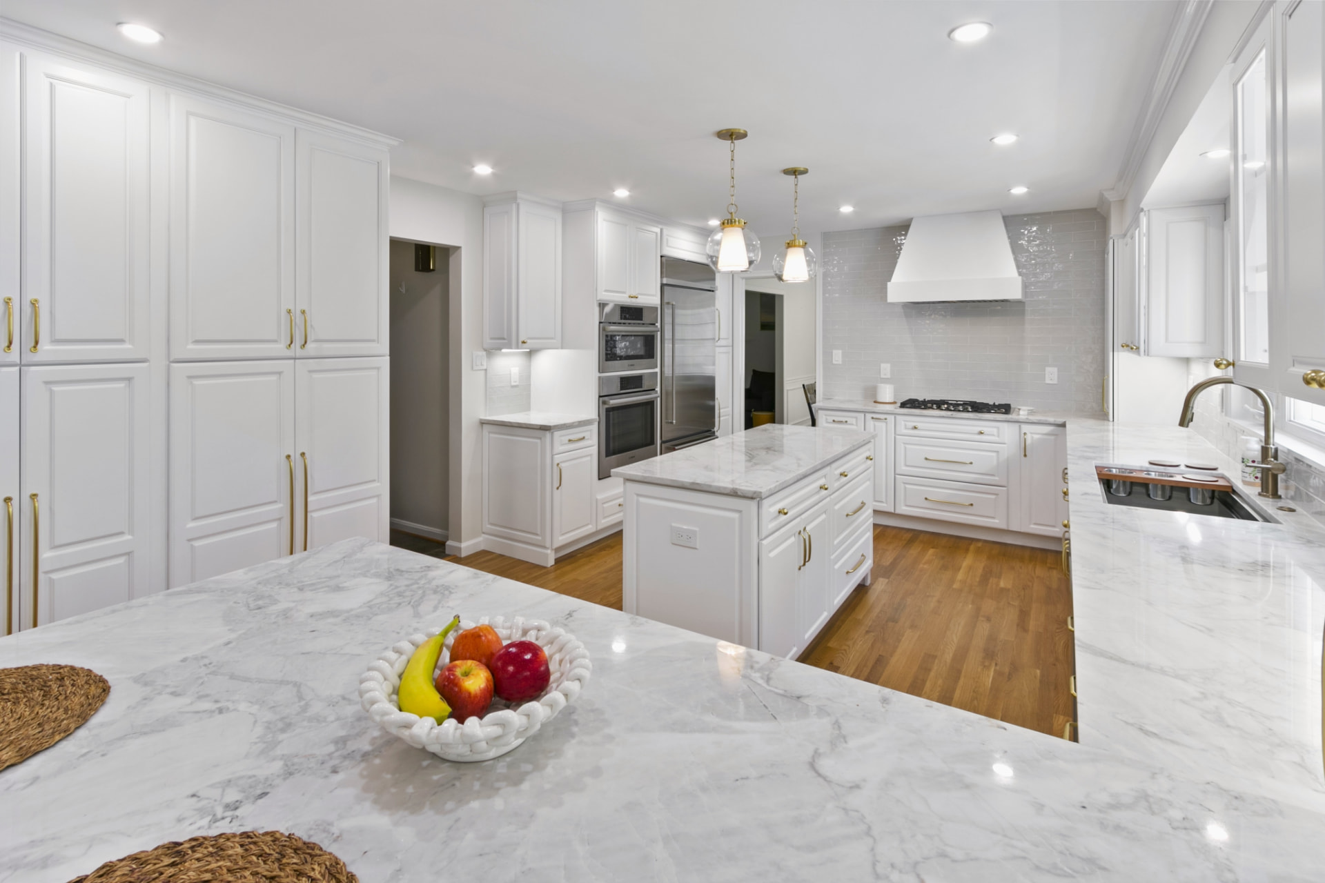 White kitchen with marble island, brass hardware and hardwood floors in Bethesda, MD