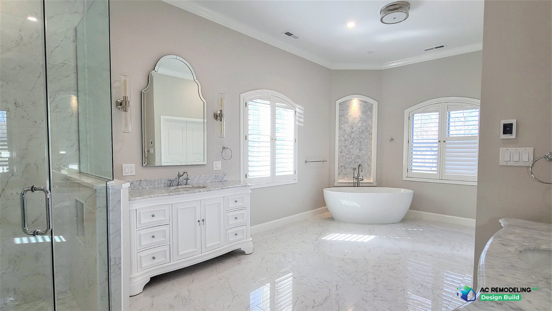 Marble primary bath with freestanding tub, white vanity and arched windows