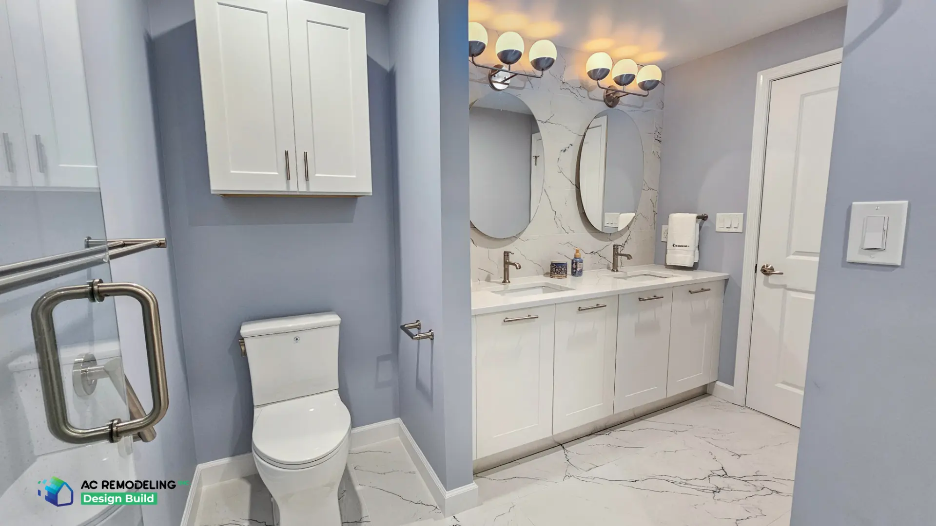 Primary bath with periwinkle walls, white shaker double vanity, oval mirrors and marble-look quartz