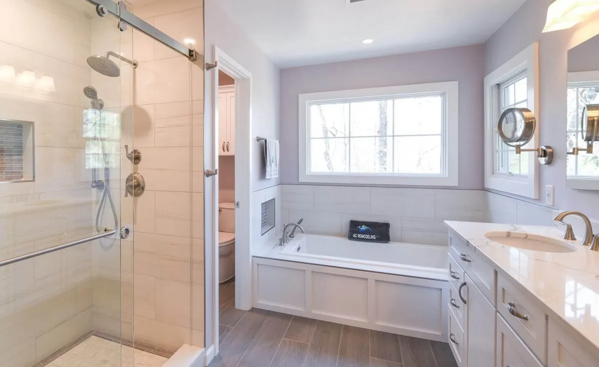 A bright and warm bathroom with a window above the tub, featuring separate areas for the toilet, shower, and tub, and a vanity sink placed in the bathroom hallway for added functionality.